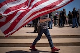 A n american flag conceals the face of a bo walking with a gun in a holster on his jeans 