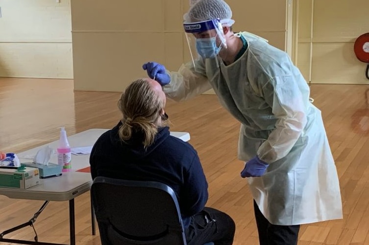 A healthcare worker in a mask, gown and shield gives a man a coronavirus test.