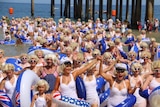 People dressed as Marilyn Monroe emerge from the sea near a jetty