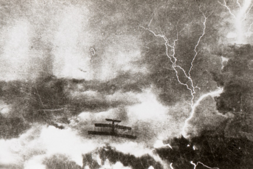An airplane flies through clouds and lightning.  The photo is old and in black and white. 