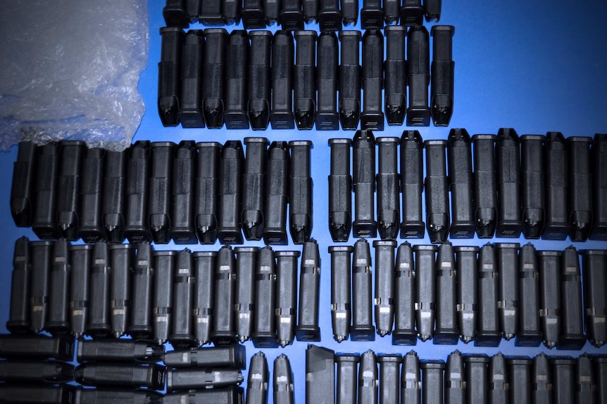 Dozens of glock pistol magazines are lined up on a blue table.