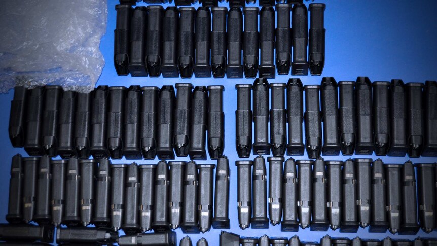 Dozens of glock pistol magazines are lined up on a blue table.