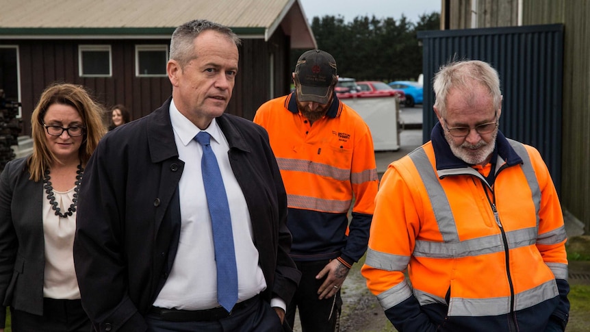 Bill Shorten, with his hands in his pockets, walks with two men in high-vis jumpers and Justine Keay