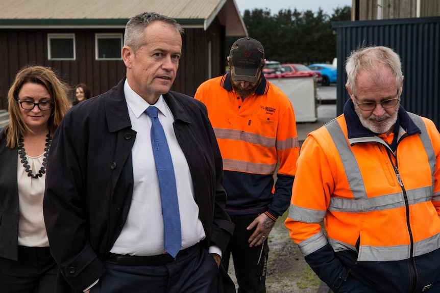 Bill Shorten, with his hands in his pockets, walks with two men in high-vis jumpers and Justine Keay