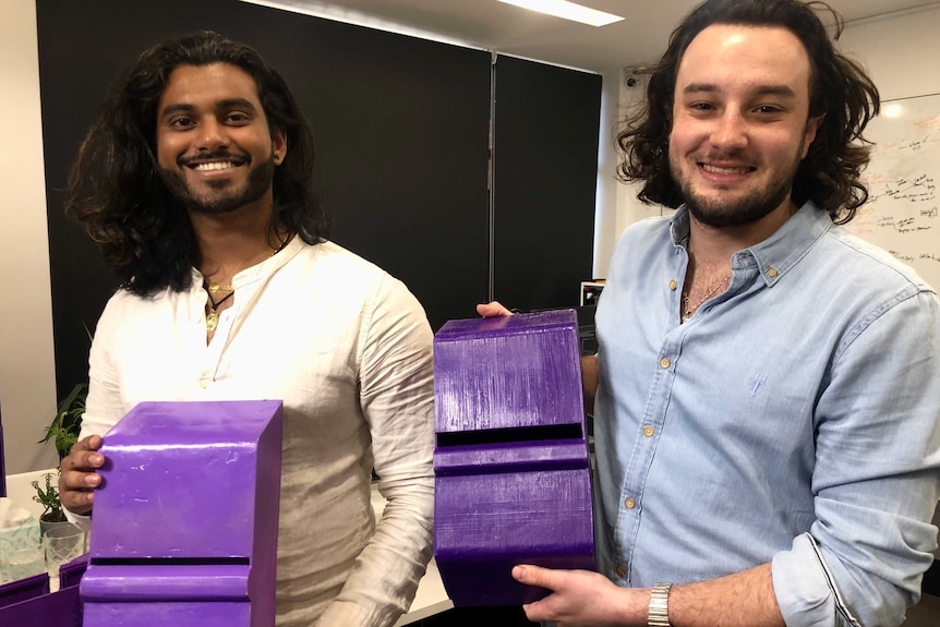Two men in a laboratory holding purple boxes