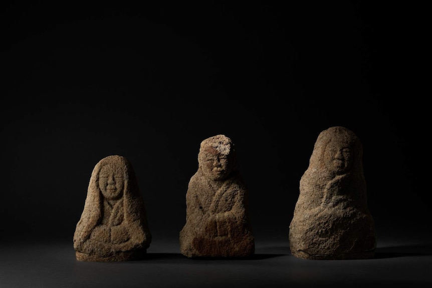 Row of three small human-shaped stone sculptures, sitting cross-legged in Buddhist poses.