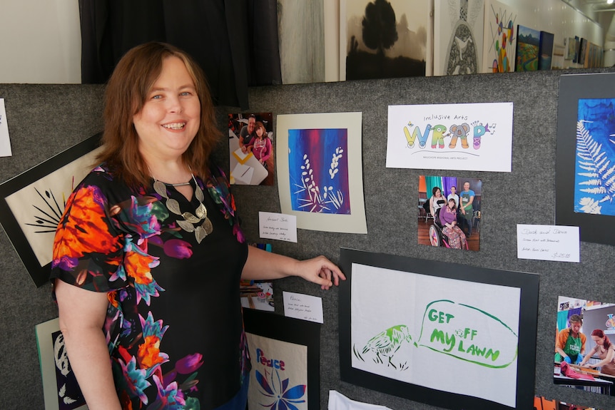 Lady in floral shirt stands in front of colorful art work. 