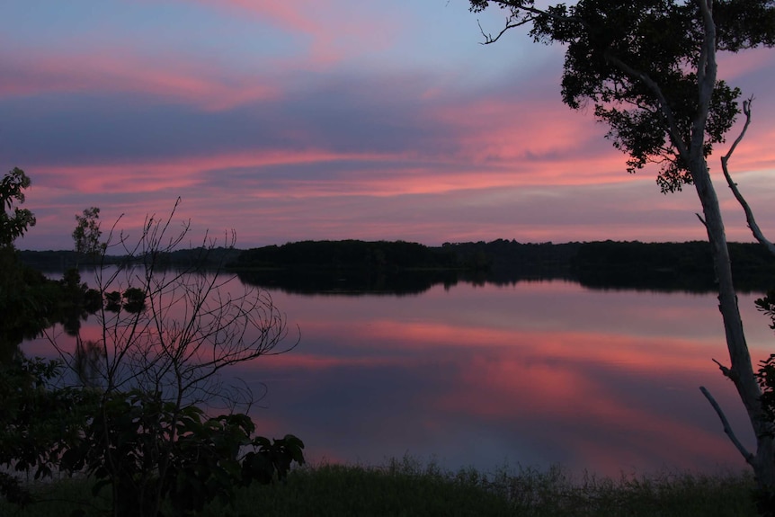 The sky glows pink over the waters of a river at sunset
