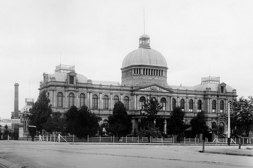 A black and white image of a stately two-story building with a tower at its centre.