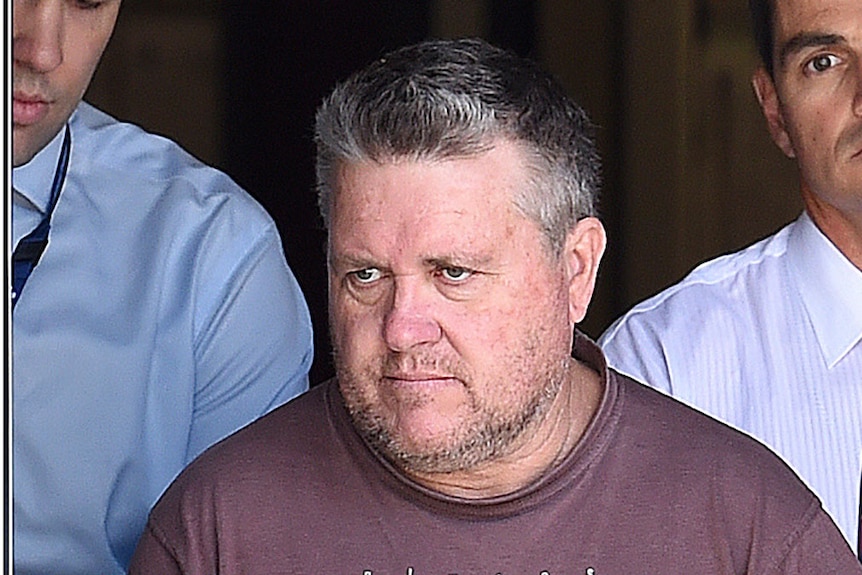 Two plain-clothes detectives escorting Rick Thorburn through the doors of a building