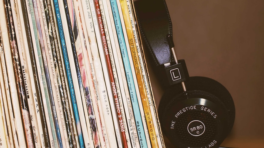 A pair of black headphones leaning against a collection of records on a shelf.