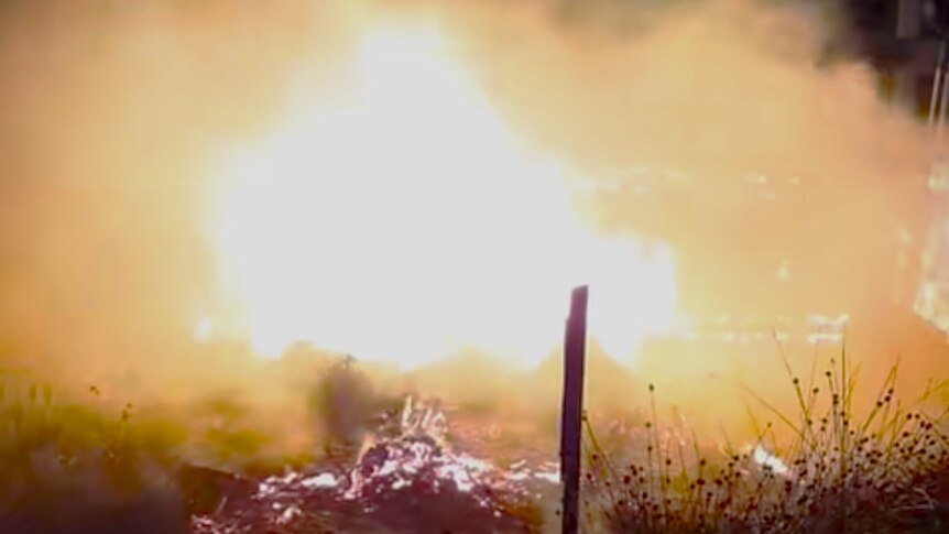 Still from video of bark hut on fire.