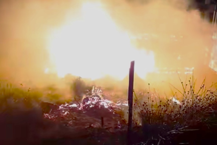 Still from video of bark hut on fire.