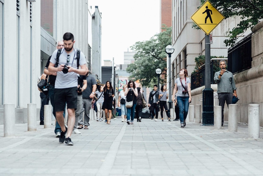 People carrying cameras and phones walk down a city laneway.