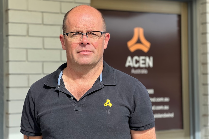 A balding man stands in front of a building