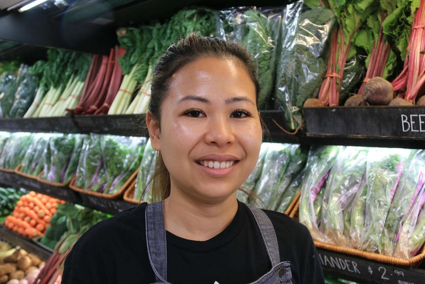 A young woman standing in front of the vegetable display.