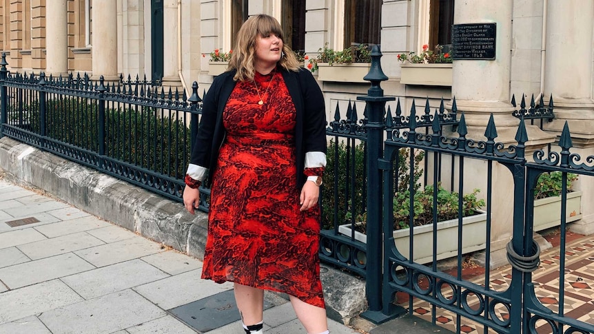 Blogger Katie Parrott wears a red dress and poses for a photo on the footpath
