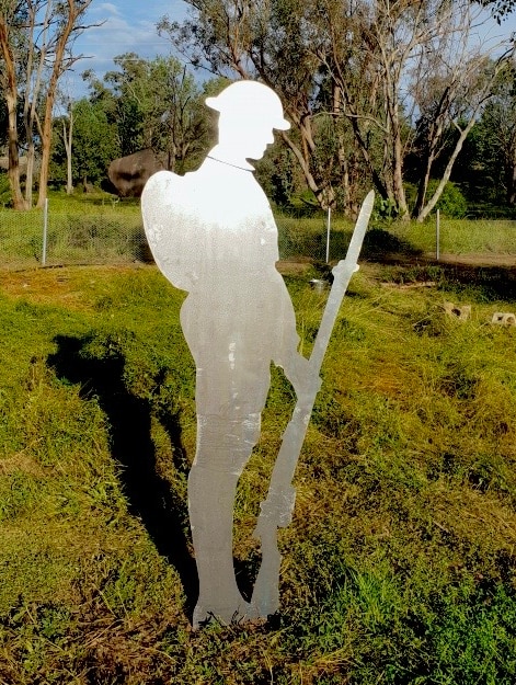 A steel cut-out of a soldier stands on grass.