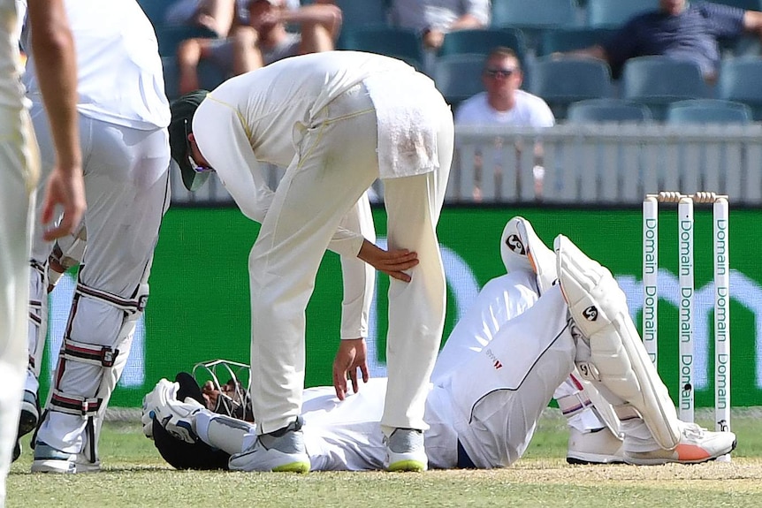 An Australian player attends to Dimuth Karunaratne as he lies injured on the ground with his helmet still on.