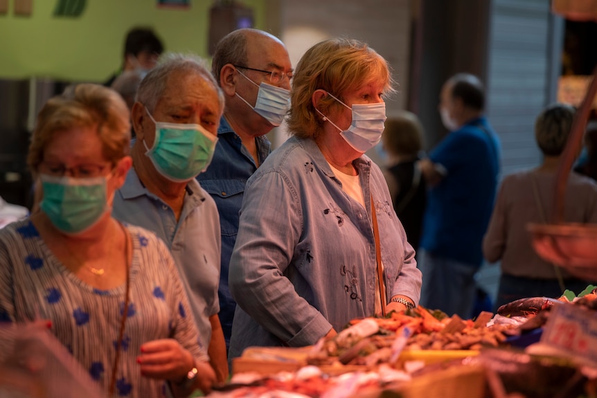 Customers wearing masks wait to be served at a fish shop in a market.