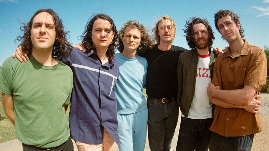 Photo of King Gizzard & The Lizard Wizard, six men standing outside in the sunshine looking at the camera