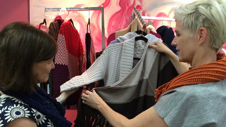 Two women hold a woollen knitted cardigan and shawl up for viewing, at a fashion show in Penrith New South Wales