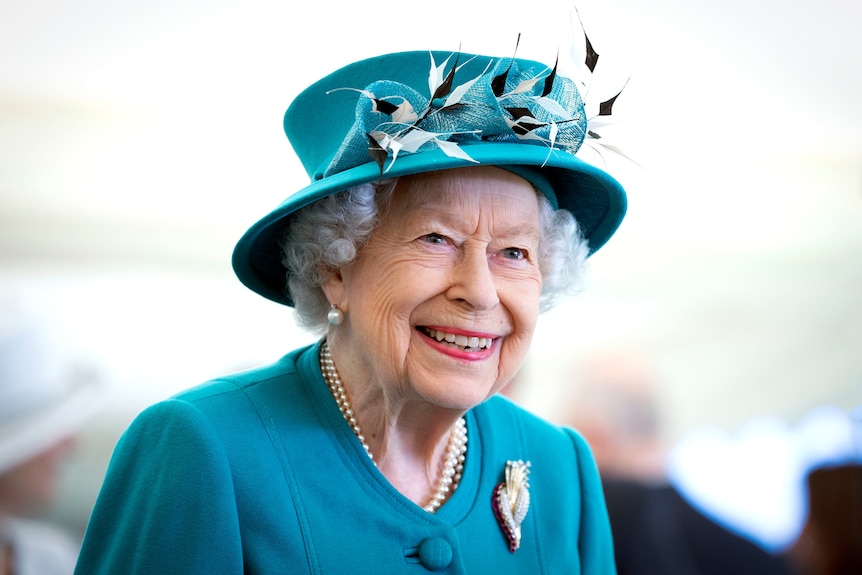 Queen Elizabeth II smiles as she wears a teal jacket and hat.