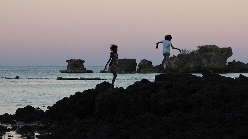 children play with a sunset beyond them