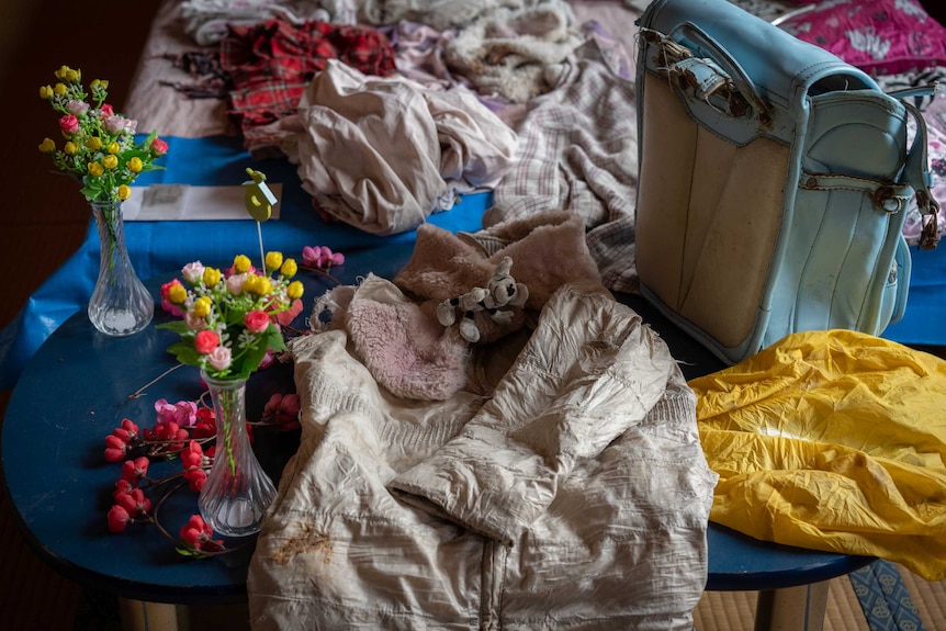 A child's scar, backpack and pink coat lie on a bed next to a vase of flowers