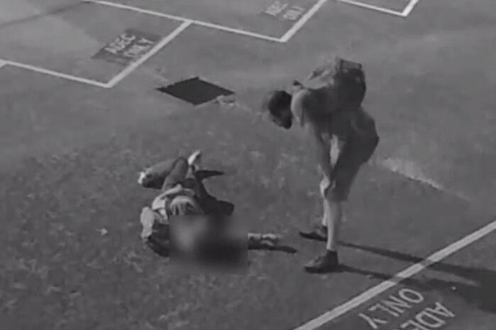 Black and white CCTV image of a man standing over another may who is on the ground.