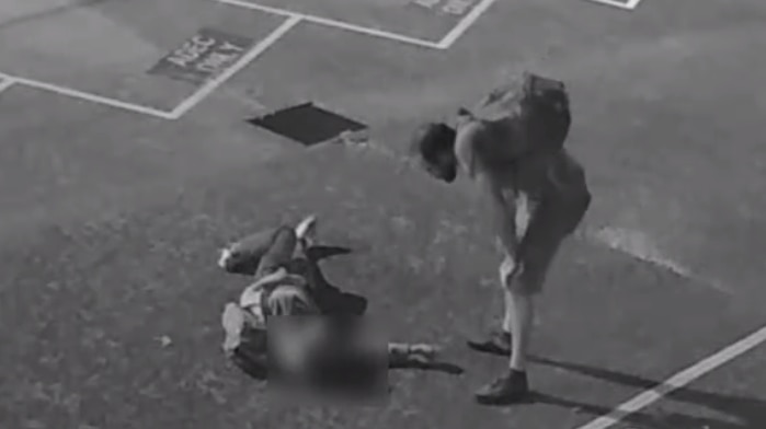 Black and white CCTV image of a man standing over another may who is on the ground.