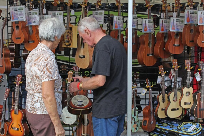 lots of ukuleles hanging in a shop with two people looking at them