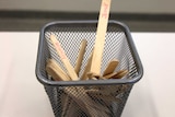 Wire basket of popsticks with names written on them sitting on a desktop.