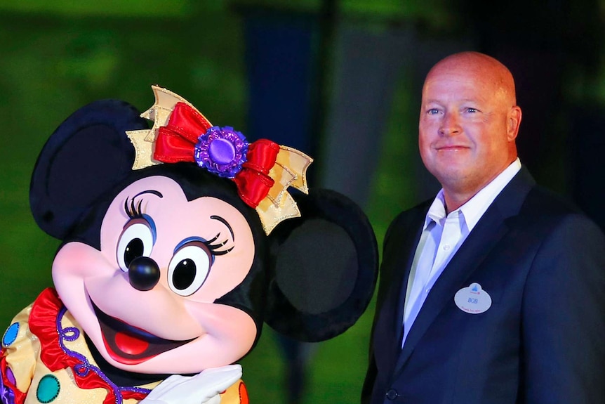 A bald man smiles and poses with Minnie Mouse.