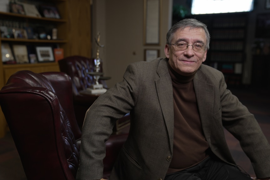 Man wearing a brown suit sitting in an office.