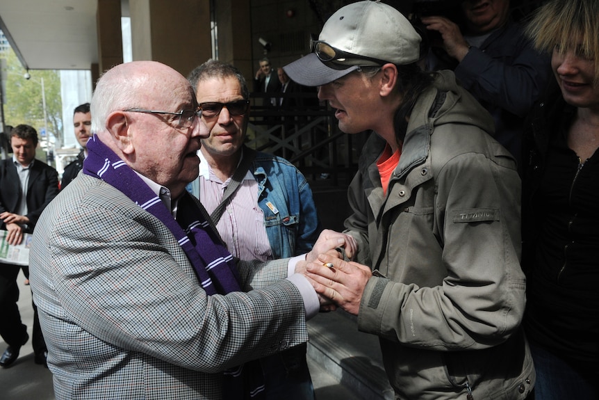 An older man shaking hands with a younger man outside a court