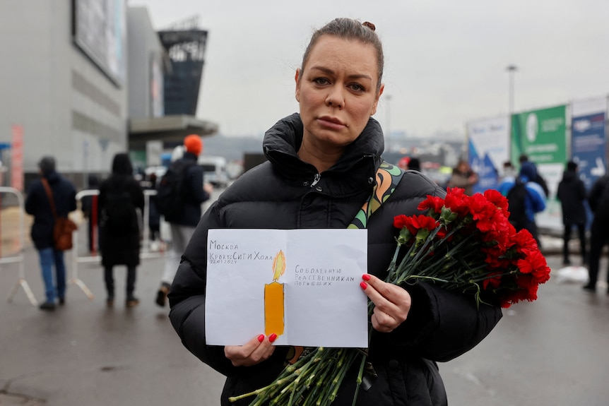 A woman holds a bunch of red flowers and a piece of paper with a drawing of a candle