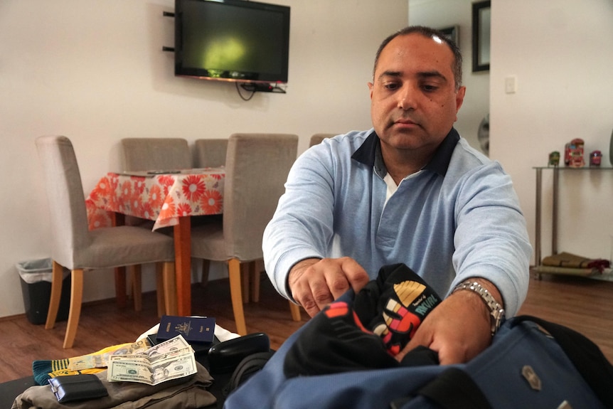 A Pakistani man in a light blue jumper is packing his bag to go on holiday.