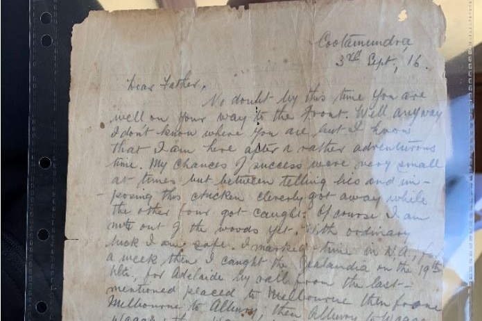 A very old letter on yellow paper is photographed inside a plastic sleeve.