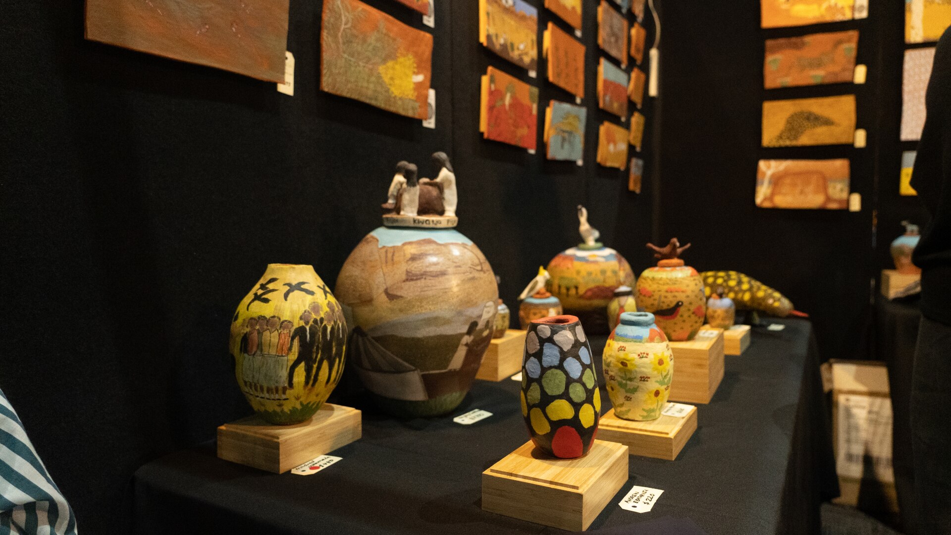 A series of painted ceramic pots on display inside an art gallery.