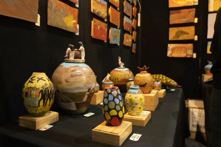 A series of painted ceramic pots on display inside an art gallery.