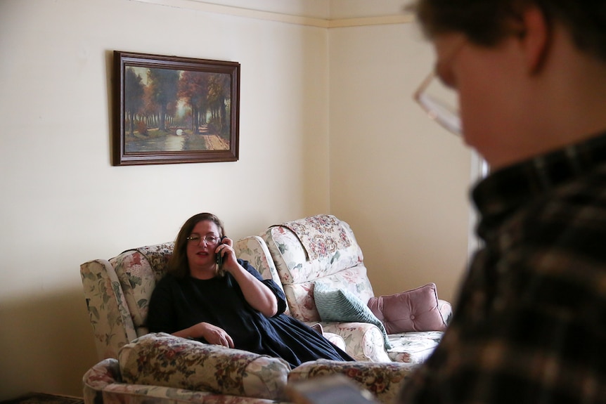 A woman talks on the phone while sitting on the couch.