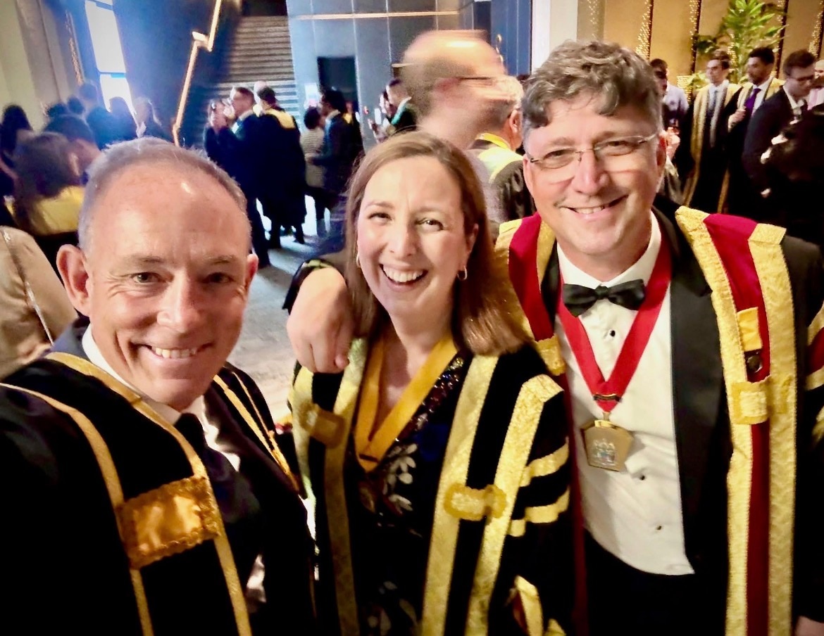 A woman stands between two men, all wearing academic robes