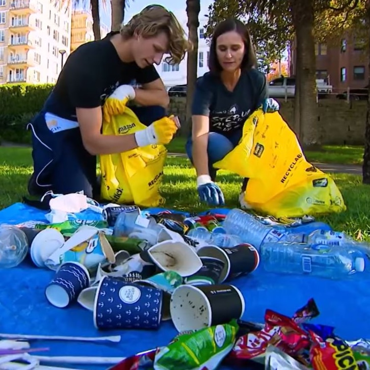 man and woman with yellow rubbish bags collecting rubbish with empty coffee cups and drink containers piled in front