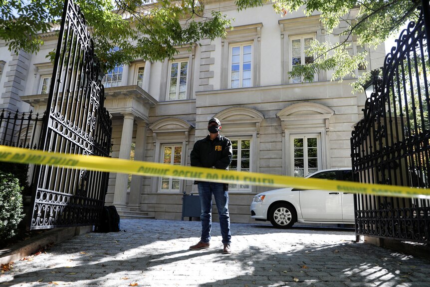 An FBI agent stands outside an upmarket property that's fenced off with yellow tape.