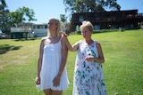 Two women in white dresses stand on a grassy hill.