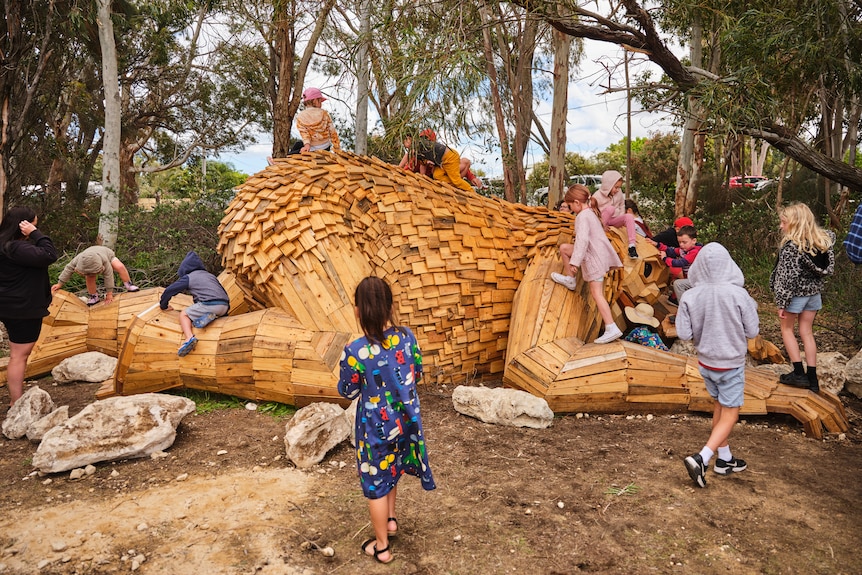 A wooden sculpture of a large giant, with children climbing all over it.