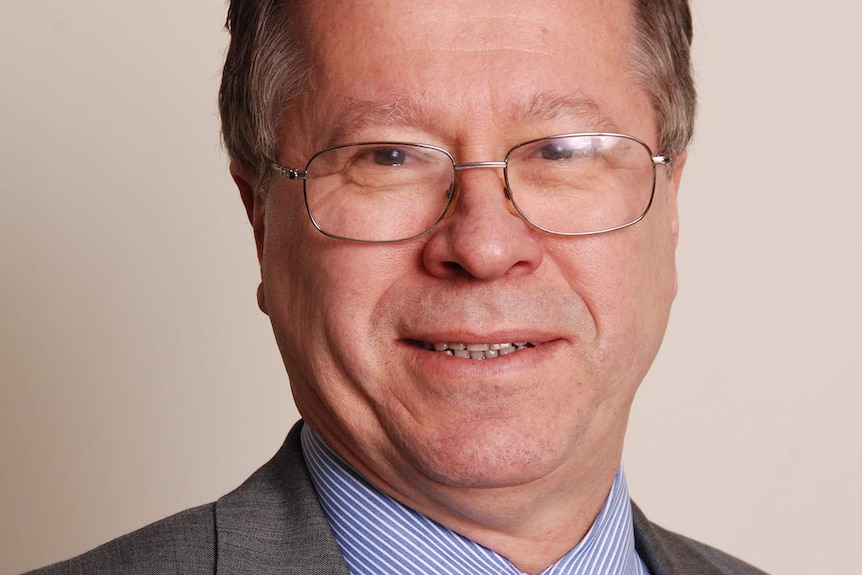 Formal portrait of a man with glasses and spectacles in a suit and tie.