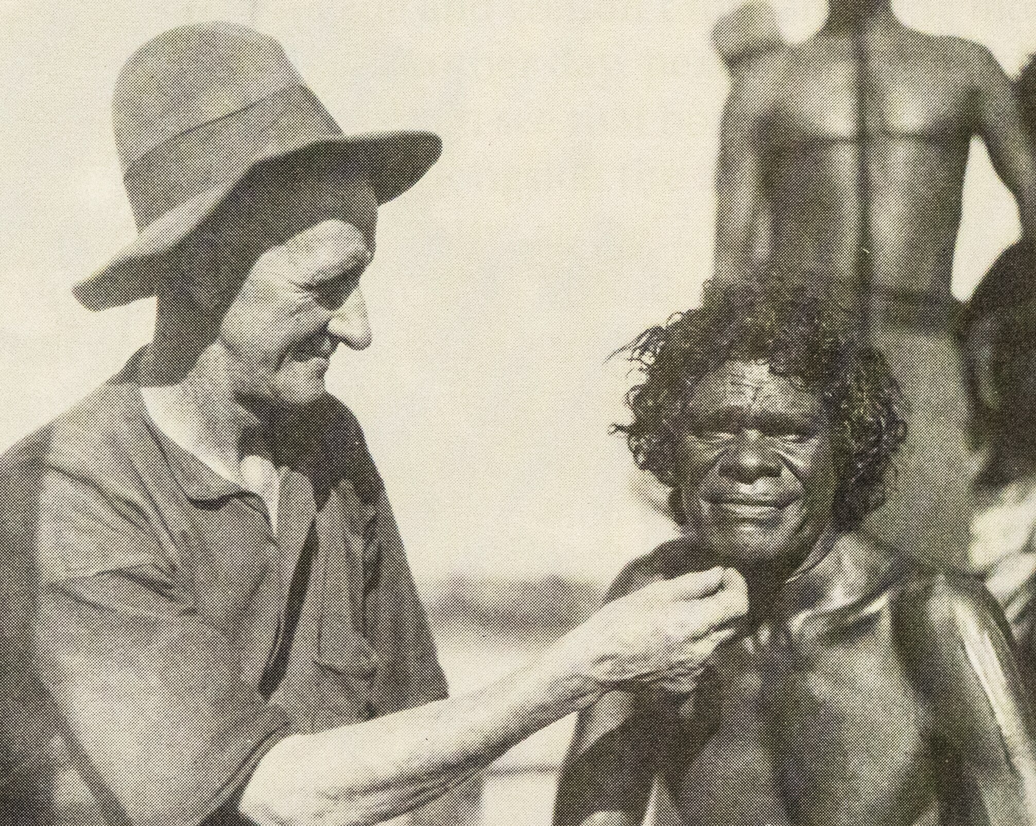 Un aborigen de piel oscura posa para la cámara mientras un hombre pone su mano debajo de su barbilla.