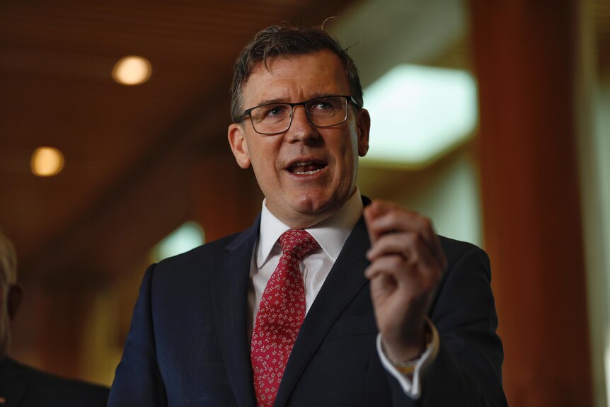 Alan Tudge wearing glasses and a suit and red tie mid-sentence using his hand to emphasise a point